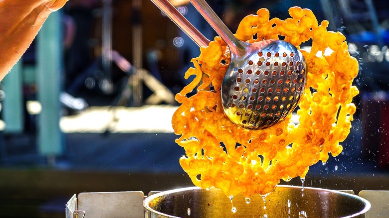 Tongs removing funnel cake from hot oil