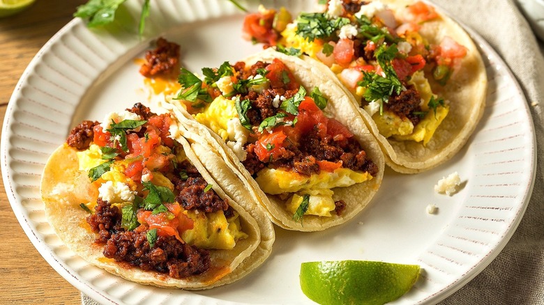 Three chorizo and egg breakfast tacos on a white scalloped plate