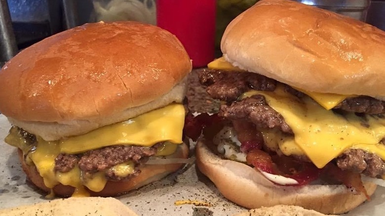 Two monstrous handheld bites of burgers with thin patties and gooey cheese.