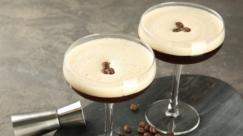 Two espresso martinis on a tray scattered with espresso beans.
