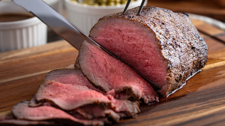 Roast beef being sliced on a wooden cutting board