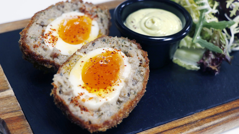 Close up of halved Scotch eggs alongside a greens salad and dipping sauce