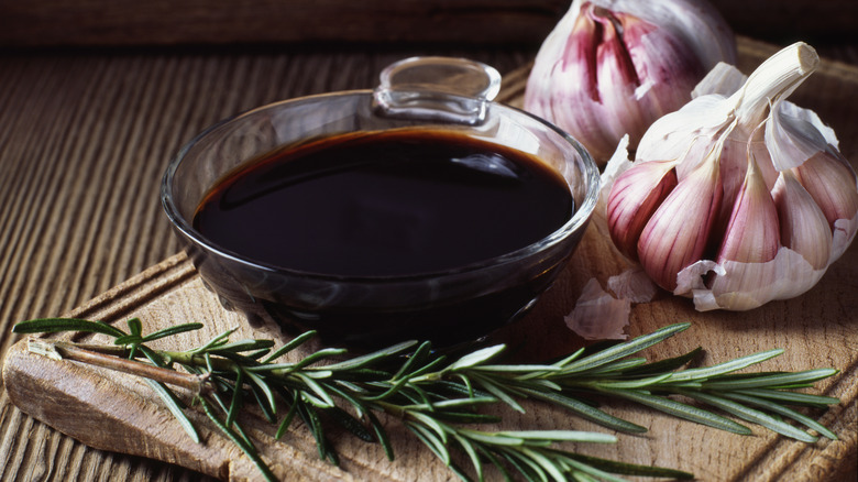 A bowl of balsamic vinegar and two garlic bulbs with fresh herbs