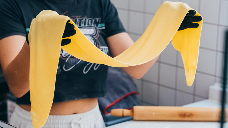 a hand holding a large sheet of rolled pasta in the kitchen