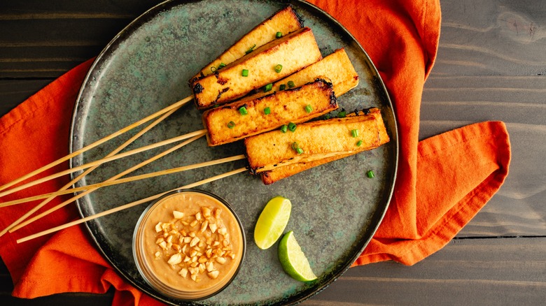 Tofu satay with a bowl of peanut sauce and wedges of lime