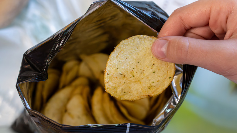 Person takes a chip from an open pack of chips