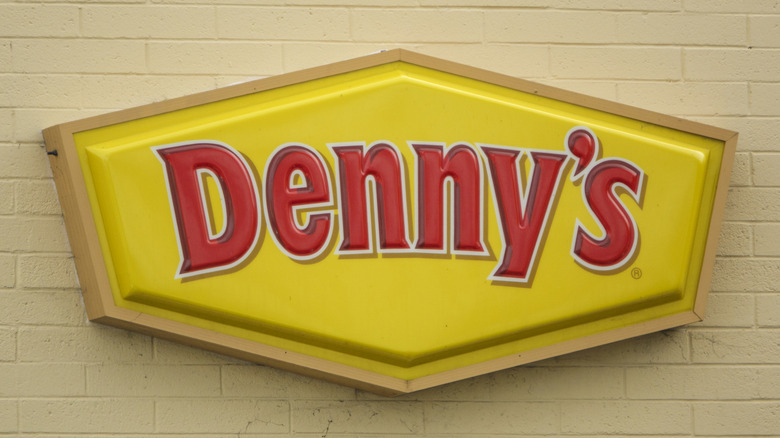 A Denny's sign on a light yellow brick wall