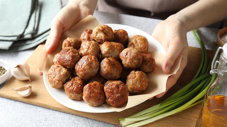 A person's hands are seen holding a plate piled with meatballs.