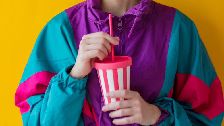 Person in a neon 80s-style jacket holding a striped soda cup