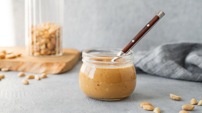a jar of homemade peanut butter with scattered peanuts