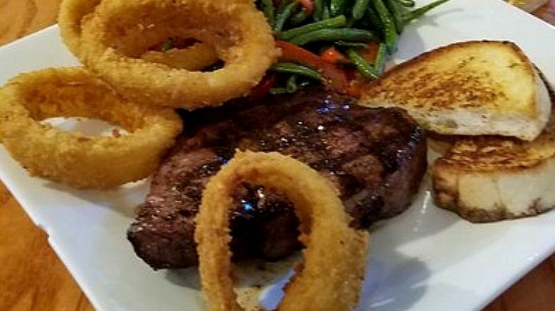 White square plate with grilled sirloin, onion rings, green beans, and toast.