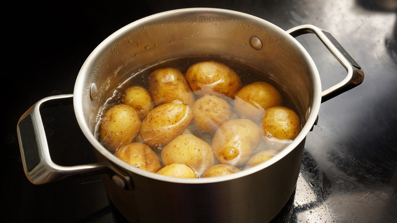 Potatoes with peel in a stainless steel pot with boiling water on the stove.