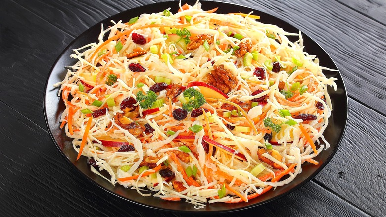 Apple cider coleslaw with walnuts, dried cranberries, and chopped green onions on a black plate