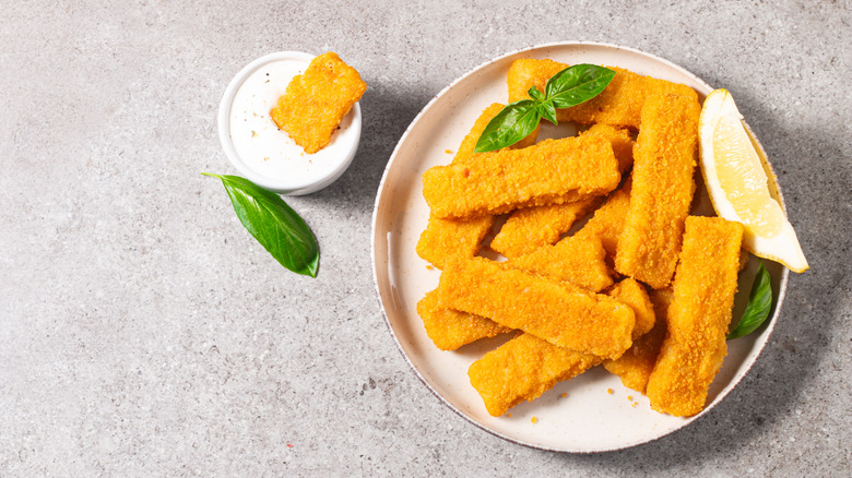 Plate of fish sticks with lemon wedge and sauce on side