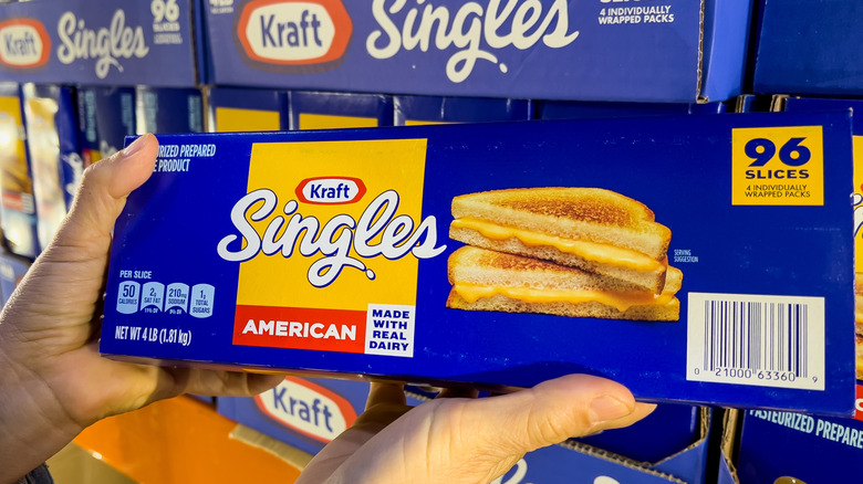 Shopper's hands holding a family-size package of Kraft's Singles Brand cheddar cheese slices.