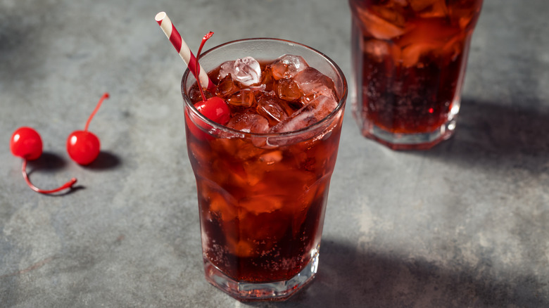 Cherry Coke in a glass with ice, cherries, and a festive red and white straw.
