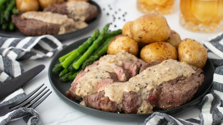 steak with cream sauce on a plate with potatoes and asparagus
