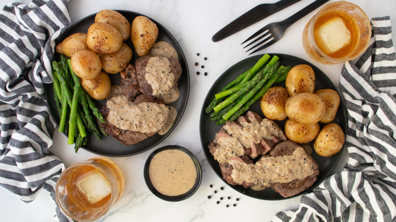 steak with cream sauce on two plates with potatoes and asparagus