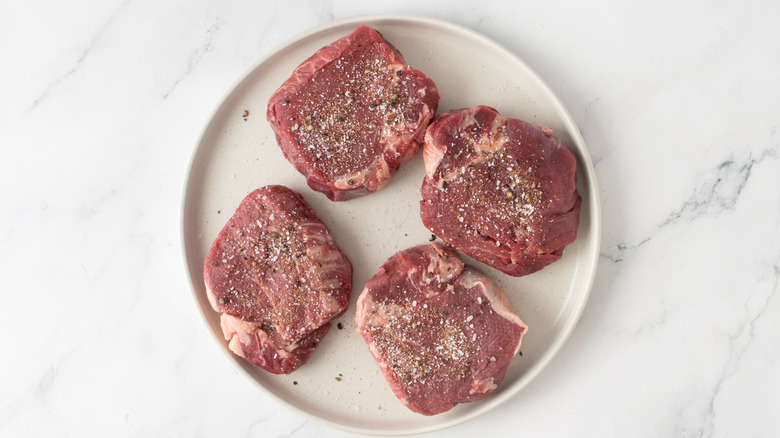 seasoned raw steaks on a white plate