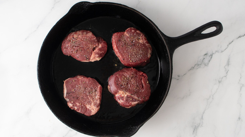 raw steaks in a black frying pan