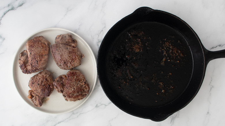cooked steaks on a white plate next to a black frying pan