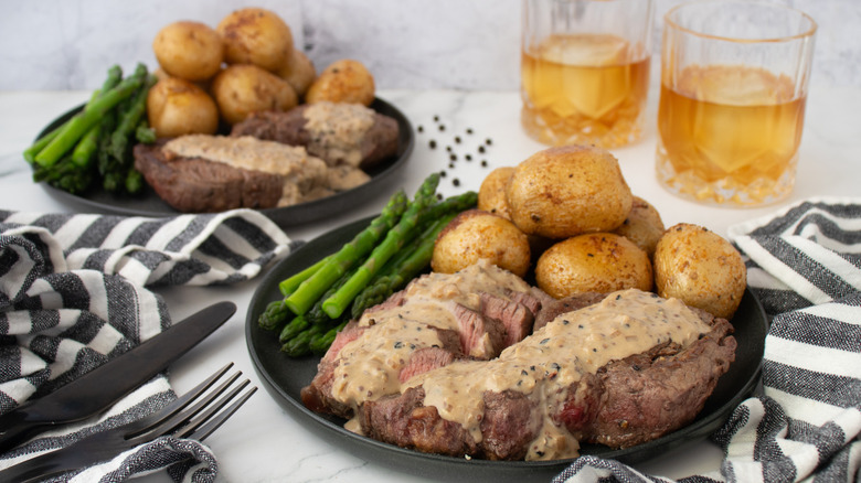 steak with cream sauce on a plate with potatoes and asparagus