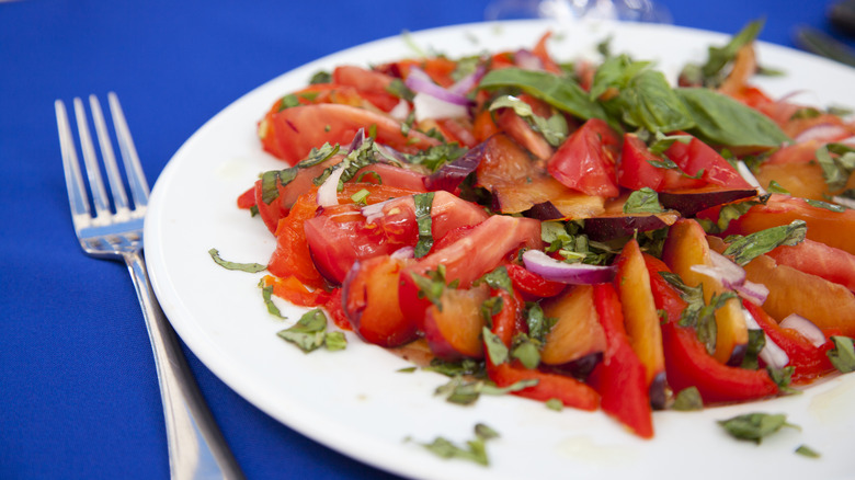 tomato and plum salad on a white plate with a fork on the side