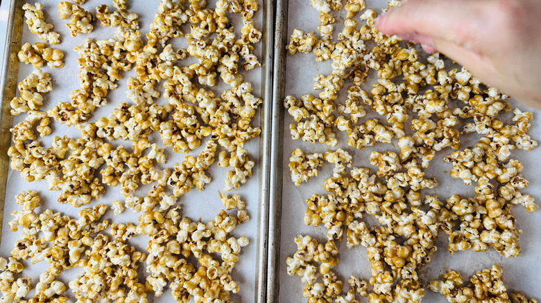 Hand sprinkling salt onto caramel popcorn on baking sheets