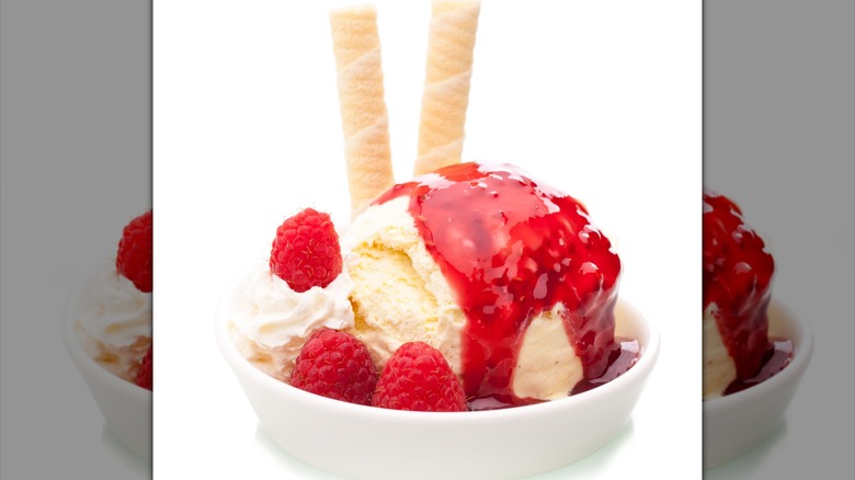 Vanilla ice cream in a bowl with raspberries, whipped cream, and wafer sticks topped with raspberry jelly