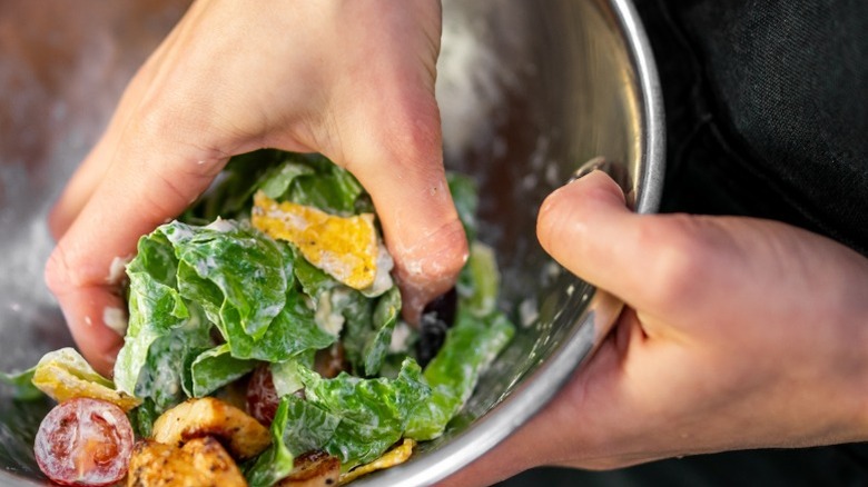 Hands mix a dressed salad in a metal mixing bowl.