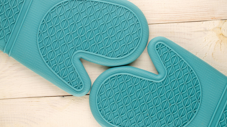 Two blue silicone oven mitts touching each other on a wooden table.