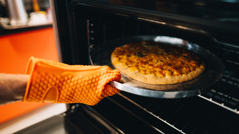 Person with an oven mitt on taking a pizza out of the oven.