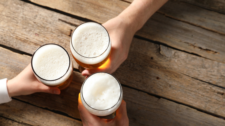 Three glasses of beer seen from above with hands reaching to grab each one.