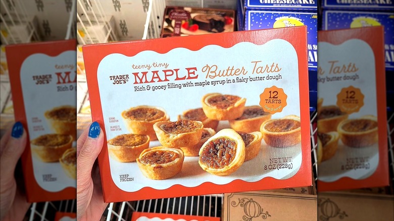 Hand with blue-painted nails holding a box of Trader Joe's Teeny Tiny Maple Butter Tarts