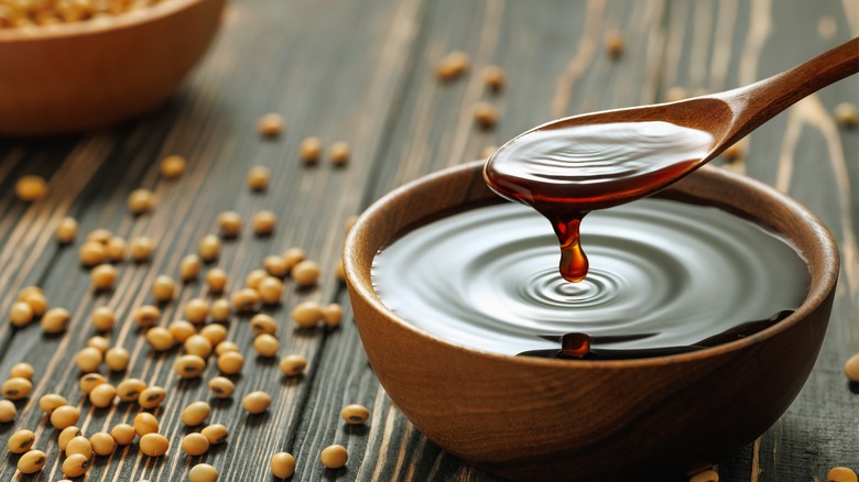 Soy sauce dish with spoon, next to soy beans on wood table.