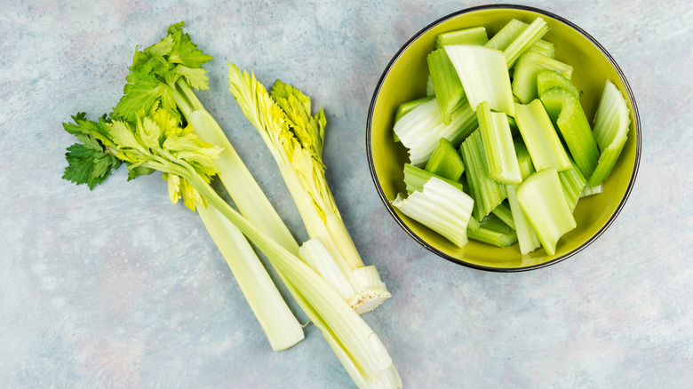 Whole celery stalks next to a bowl of chopped celery on a counter.