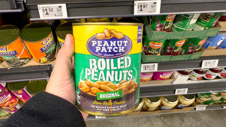 Person holding a can of boiled peanuts in grocery store aisle