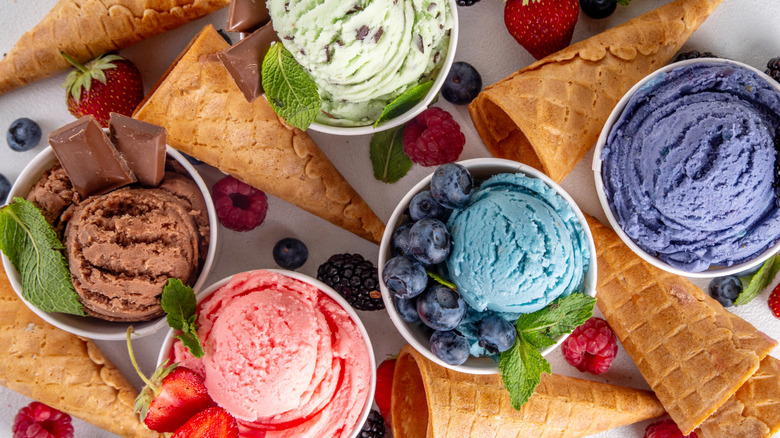 Cups filled with different flavors of ice cream surrounded by waffle cones.