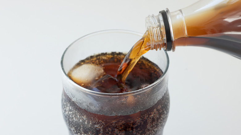 Soda from two-liter bottle being poured into glass with ice