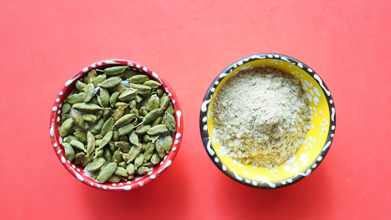 A bowl of cardamom pods and a bowl of ground cardamom next to each other.