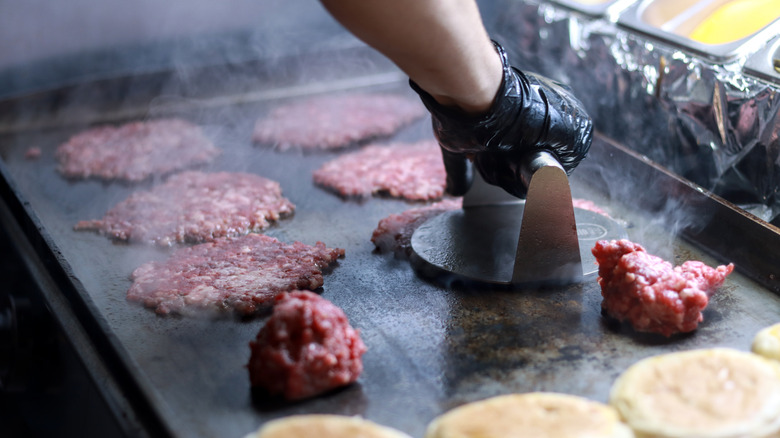 a cook smashes a burger while frying