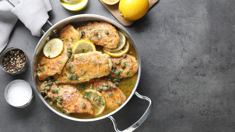 Chicken picatta is arranged in a pan with lemon slices and capers.