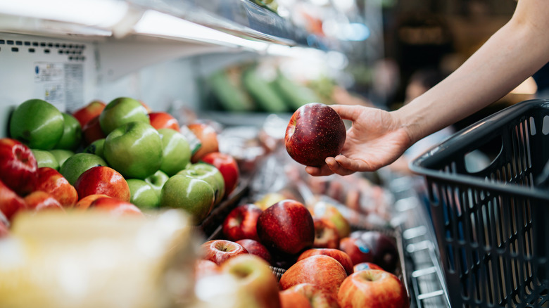 A hand picking up a red apple from a grocery store display