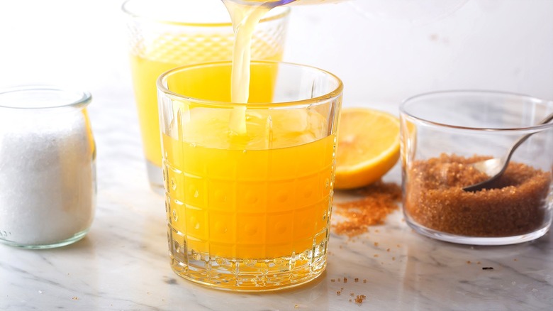 Clear glass of combined lemon and orange juice next to bowls of brown sugar and salt