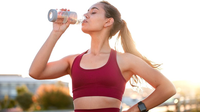 Woman in workout clothes drinking from a reusable bottle outside