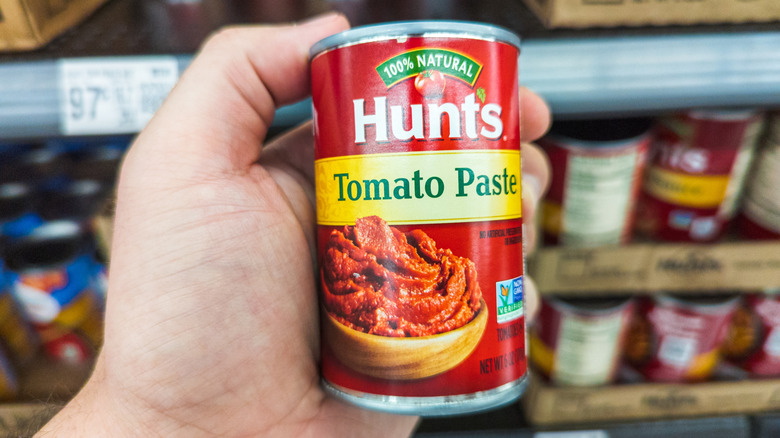 A hand holding a can of tomato paste in grocery store aisle