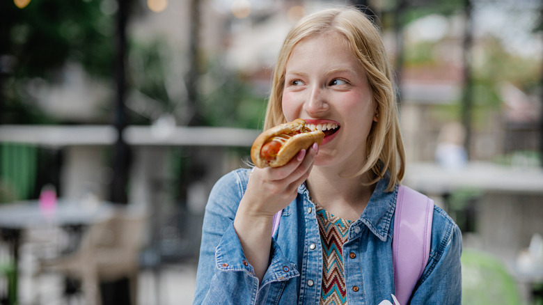 A young woman smiling while eating a hot dog