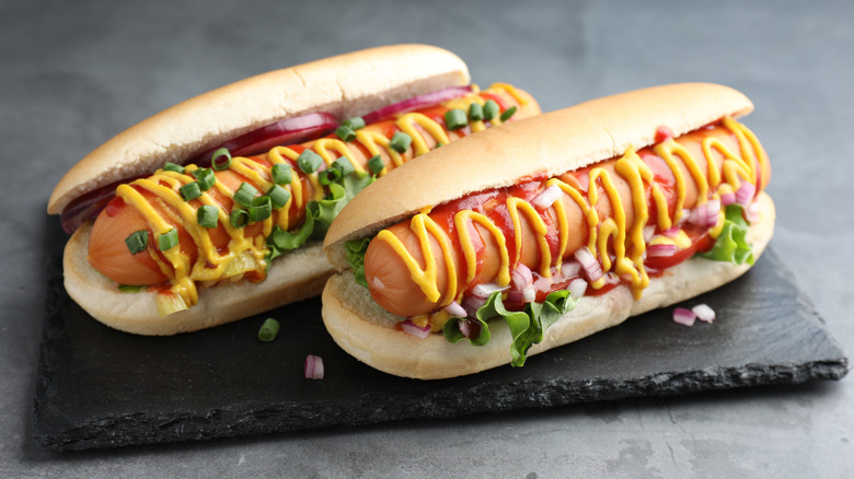 Close -p of hot dogs with sauces, lettuce, and onion on grey textured table