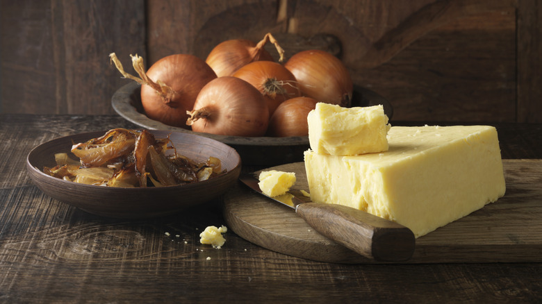 A bowl of whole, raw onions, a block of butter, and a dish of caramelized onions.