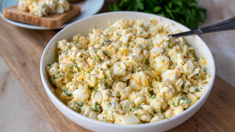 Egg salad in a bowl on a chopping board with toast in the background
